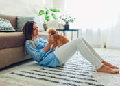 Thumbnail 7 of 9 - A woman in a blue shirt is sitting on a rug with her orange cat.