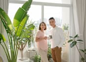 Thumbnail 6 of 9 - A man and woman standing in a room with a large window and plants.