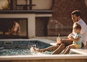 Thumbnail 3 of 18 - A man and a child are sitting by a pool.