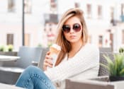 Thumbnail 5 of 9 - A woman in a white sweater and blue jeans is sitting on a chair holding an ice cream cone.