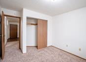 Thumbnail 15 of 18 - A room with a carpeted floor and a white wall with a door and a closet. Fargo, ND Cedars 4 Apartments