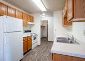 Thumbnail 20 of 44 - A kitchen with a white refrigerator, wooden cabinets, and a sink. Fargo, ND Country Edge Apartments