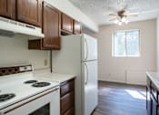 Thumbnail 14 of 21 - A kitchen with a white refrigerator, white stove, and wooden cabinets. Bismarck, ND Belmont Apartments