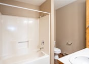 Thumbnail 10 of 13 - A white bathtub with a shower head and a white sink with a brown cabinet.
