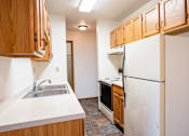 Thumbnail 8 of 17 - A kitchen with wooden cabinets and a white refrigerator. Fargo, ND Southgate Apartments