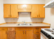 Thumbnail 3 of 7 - A kitchen with wooden cabinets and a white stove top oven. Fargo, ND Birchwood Apartments
