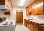 Thumbnail 29 of 34 - A kitchen with a white stove and wooden cabinets. Fargo, ND Islander Apartments