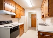 Thumbnail 28 of 34 - A kitchen with wooden cabinets and a white stove top oven. Fargo, ND Islander Apartments