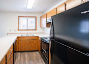 Thumbnail 8 of 42 - A black refrigerator is in the corner of a kitchen with wooden cabinets. Fargo, ND Westwood Estates