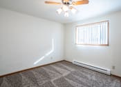 Thumbnail 16 of 20 - A room with a ceiling fan, a window with blinds, and a carpeted floor. Fargo, ND Kennedy Apartments