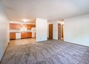 Thumbnail 19 of 21 - A room with a carpeted floor and a kitchen area in the background. Fargo, ND West Oak Apartments