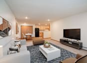 Thumbnail 7 of 46 - A modern living room with a white couch, a coffee table, and a flat-screen TV. Grand Forks, ND Cherry Creek Apartments