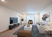 Thumbnail 8 of 46 - A living room with a white couch, a brown ottoman, a television, and a plant. Grand Forks, ND Cherry Creek Apartments