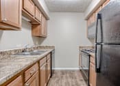 Thumbnail 25 of 34 - A kitchen with a black refrigerator, brown cabinets, and a granite countertop. Omaha, NE Evergreen Terrace Apartments