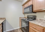 Thumbnail 27 of 34 - A kitchen with a black stove top oven and microwave above it. Omaha, NE Evergreen Terrace Apartments