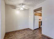 Thumbnail 18 of 29 - A room with a ceiling fan and a kitchen in the background. Omaha, NE Stony Brook Apartments