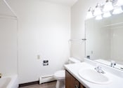 Thumbnail 20 of 23 - A white bathroom with a toilet, sink, and mirror. West Fargo, ND Parkwest Gardens