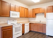 Thumbnail 11 of 24 - A kitchen with wooden cabinets and white appliances. Fargo, ND North Sky II Apartments