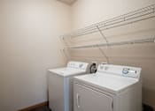 Thumbnail 17 of 24 - Two white front loading washing machines in a laundry room. Fargo, ND North Sky II Apartments