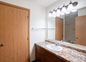 Thumbnail 23 of 25 - A bathroom with a sink, mirror, and wooden door. Fargo, ND Park Place Apartments