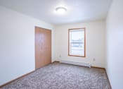 Thumbnail 16 of 25 - A room with a carpeted floor, a door, a window, and a small radiator. Fargo, ND Park Place Apartments