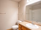Thumbnail 19 of 20 - A bathroom with a toilet, sink, mirror, and towel rack. Fargo, ND East Bridge Apartments