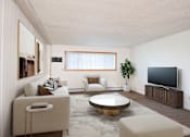 Thumbnail 1 of 14 - A living room with a white couch, a brown armchair, a coffee table, and a television. Fargo, ND Park Terrace Apartments