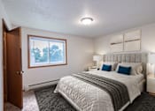 Thumbnail 5 of 14 - A bedroom with a large bed and a window overlooking trees. West Fargo, ND Clearview Apartments