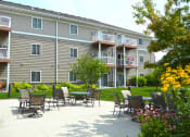 Thumbnail 1 of 21 - The exterior of a three level apartment building with a grass and patio area out front. Fargo, ND Crossroads Apartments