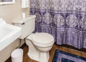 Thumbnail 5 of 7 - Grand Forks, ND Barrette Arms Apartments. a bathroom with a white sink and toilet and a purple and white shower curtain