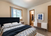 Thumbnail 2 of 10 - Bismarck, ND Brandon Apartments  a bedroom with a large bed, a blue and white comforter, a large window, and walk-in closet.