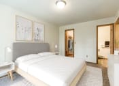 Thumbnail 4 of 10 - Bismarck, ND Brandon Apartments. The room showcases a comfortable bed with neatly arranged bedding and a calm ambiance. Soft lighting adds to the peaceful atmosphere, while a window allows natural light to fill the space. It's a tranquil retreat for rest and relaxation.