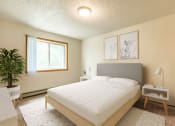 Thumbnail 3 of 10 - Bismarck, ND Brandon Apartments. The room showcases a comfortable bed with neatly arranged bedding and a calm ambiance. Soft lighting adds to the peaceful atmosphere, while a window allows natural light to fill the space. It's a tranquil retreat for rest and relaxation.