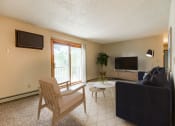 Thumbnail 1 of 10 - Bismarck, ND Brandon Apartments. A living room with a couch and a chair. A large sliding glass door allows natural light to fill the room.