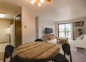 Thumbnail 4 of 14 - Bismarck, ND Eagle Sky I. A dining room with a four chair table. a living room with a couch, coffee table, and a flat screen tv in the background. The glass sliding door in the living room brightens the room with natural light.