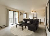 Thumbnail 1 of 14 - Bismarck, ND Eagle Sky I Apartments. a living room with a large couch and a coffee table in front of a sliding glass door that brightens the room