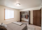 Thumbnail 5 of 16 - A bedroom with a bed and a closet with clothes in it. Bismarck, ND Eastbrook Apartments.