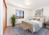 Thumbnail 3 of 13 - Bismarck, ND Fairview Apartments. A bedroom that showcases a comfortable bed with neatly arranged bedding, a stylish bed bench, and a window that fills the space with natural light. It's a serene and inviting setting for rest and relaxation.