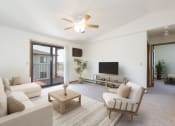 Thumbnail 1 of 13 - Bismarck, ND Fairview a living room with white walls and a sliding glass door to a balcony. The furniture is a bright white such as the couch and chair.