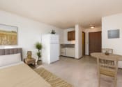 Thumbnail 5 of 7 - Mandan, ND Garden Grove Apartments. A bedroom area in a studio with a bed a table and a chair and a refrigerator