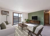 Thumbnail 1 of 7 - Mandan, ND Garden Grove Apartments. A living room with green walls and a sliding glass door to a balcony