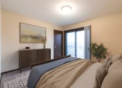 Thumbnail 5 of 10 - Bismarck, ND Newgate Apartments.  a bedroom with a large bed and a dresser. A glass sliding door brightens with room with natural light.