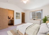 Thumbnail 5 of 11 - Bismarck Pebble Creek Apartments.  a bedroom with a large bed and a bathroom in the background. a large window fills the room with natural light