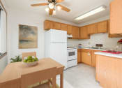 Thumbnail 4 of 10 - Bismarck, ND Riverpark Apartments a kitchen with white appliances and a wooden table with a bowl of fruit on it. The natural light from the window next to the table brightens the room