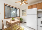 Thumbnail 3 of 10 - Bismarck, ND Riverpark Apartments a kitchen with white appliances and a wooden table with a bowl of fruit on it. The natural light from the window next to the table brightens the room