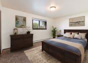 Thumbnail 4 of 17 - Bismarck, ND Rosser Apartments. A bedroom with dark wood bed, dresser, and night stands. A small window fills the room with natural light