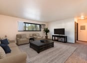 Thumbnail 1 of 17 - Bismarck, ND Rosser Apartments. A living room with couches, a coffee table, and a tv. A long window fills the room with bright natural light