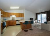 Thumbnail 3 of 26 - a kitchen with white appliances and wooden cabinets. Theres a living room in the background with a gray accent wall. Fargo, ND Bridgeport Apartments