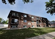 Thumbnail 9 of 10 - a brick apartment building with a lawn and a blue sky
