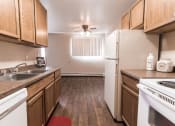 Thumbnail 14 of 19 - Grand Forks, ND Cherry Creek Apartments. A kitchen in the unit 110 with wood floors an white appliances with a dining room in the background that has a window